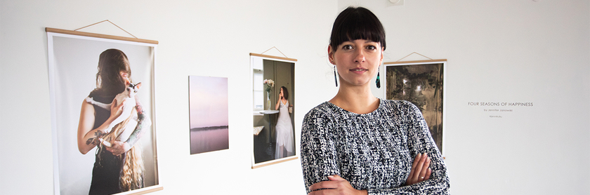 Jennifer Janowski steht vor Fotografien ihrer Ausstellung die an einer weißen Wand hängen